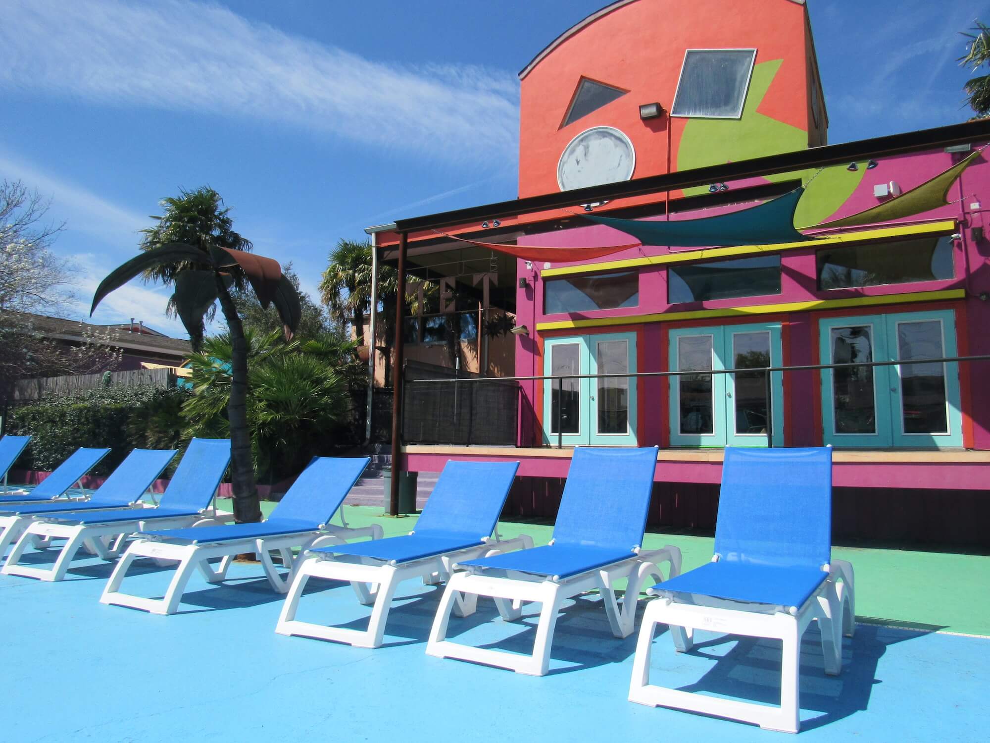 The outdoor pool area of The Metropolis Apartments with many blue pool chairs