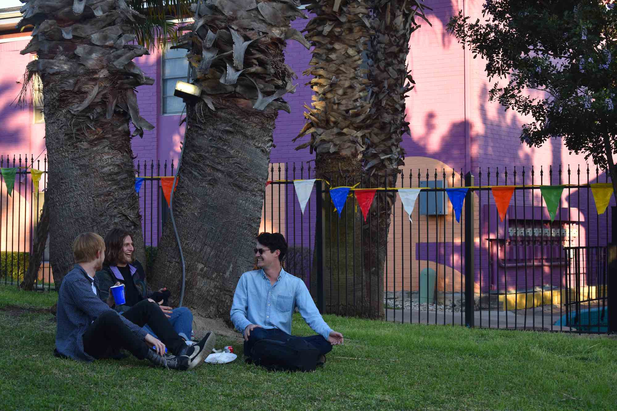 A group of friends sit on grass, beside a tree