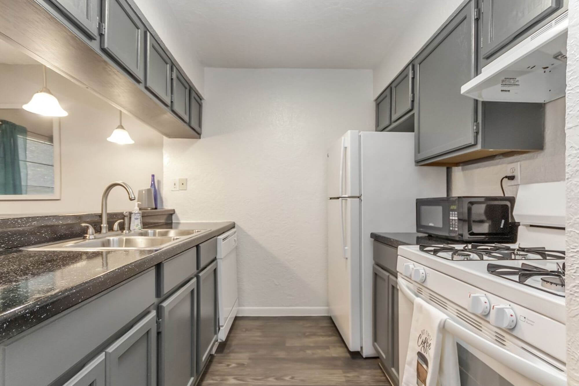 The kitchen view of The Metropolis Apartments with gray cabinets and white appliances